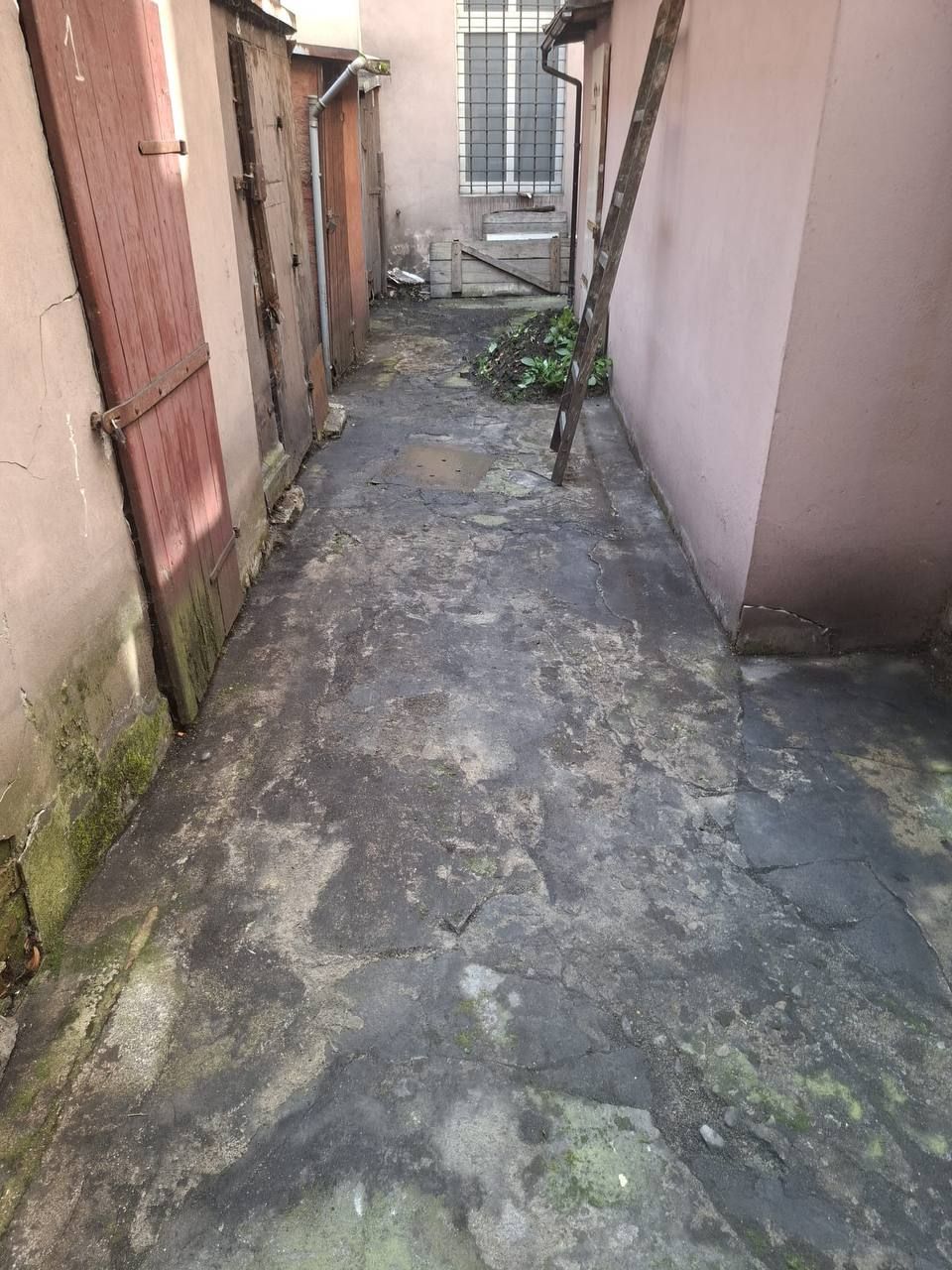 Wąskie przejście między budynkami z zabrudzoną nawierzchnią